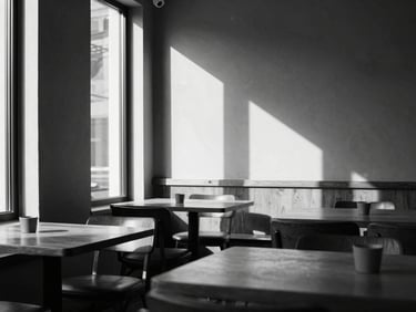 Clean architectural shot of a monochrome café interior, strong shadows, warm natural light filtering through tall windows, minimalist table settings, 35mm lens.