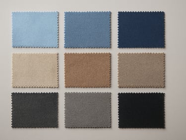 Wide flat overhead shot of fabric material swatches organized in a grid by category — synthetics in cool blues, natural blends in warm taupes, technical weaves in charcoal — on a neutral light grey surface under diffused north-facing studio light, edges of swatches sharp and color-accurate
