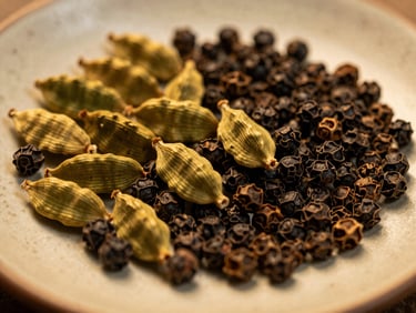 Macro shot of whole black peppercorns, green cardamom pods, and golden turmeric roots on a textured ceramic plate, warm golden lighting.