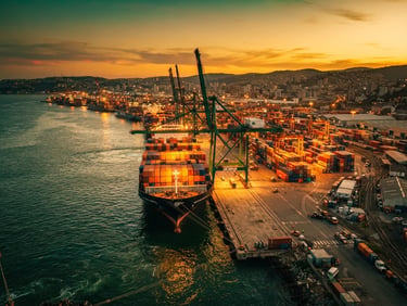 Wide cinematic shot of a deep-water port at dusk, cargo ships lined up, dramatic golden hour lighting, rich emerald tones, 35mm