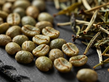 Macro close-up of raw green coffee beans and premium dried tea leaves arranged neatly on a dark slate surface, dramatic side lighting, shallow depth of field.