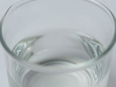 Close-up macro shot of liquid viscosity in a glass beaker, showing subtle texture and light refraction, clean neutral studio lighting, cool desaturated tones, sharp focus, shallow depth of field, clinical aesthetic