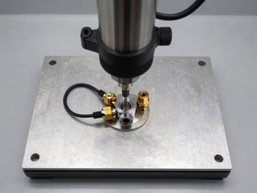 Overhead flat-lay shot of a press-fit and leak-test machine fixture plate, hydraulic press cylinder above, air-decay test fittings connected to component port, crisp overhead shop-floor task lighting, steel and aluminium components sharp in frame