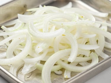 Close-up of uniform white onion flakes on a clean stainless steel tray, diffused studio light, emphasizing texture
