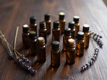 Overhead shot of a small collection of amber glass essential oil bottles and dried lavender sprigs on a dark wooden surface, soft warm light from the side, deep shadows.