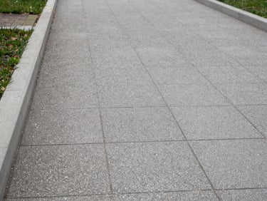 Close documentary shot of a paved pedestrian pathway with concrete edging markers at a horizontal condominium, overcast daylight, no people, precise framing showing lot boundary lines