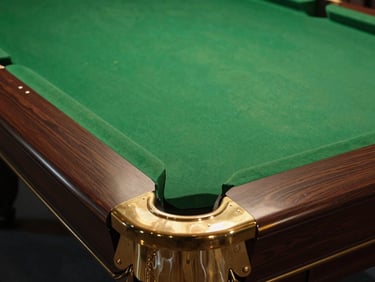 Polished brass pocket corners on a dark wood billiard table, warm overhead table lamp casting sharp shadows, 35mm