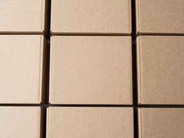 Overhead shot of neatly stacked flat-laid folding cardboard boxes, raw kraft brown tones, clean minimalist composition