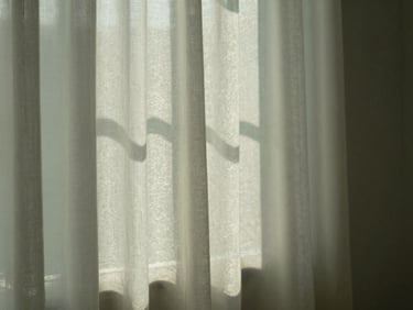 Soft morning sunlight filtering through a sheer curtain, casting gentle patterns on a warm textured wall