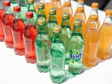 Chilled Sprite and Fanta bottles arranged neatly on a clean white surface, bright daylight, vibrant green and orange tones, sharp focus, 35mm