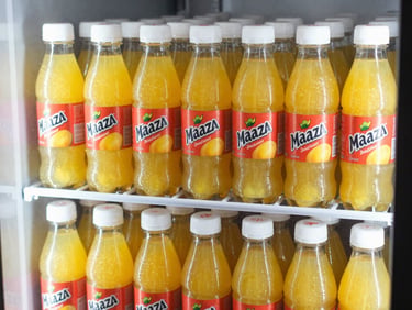 Bottles of Maaza mango drink stacked in a retail cooler, bright natural lighting, rich yellow tones, sharp focus, 35mm