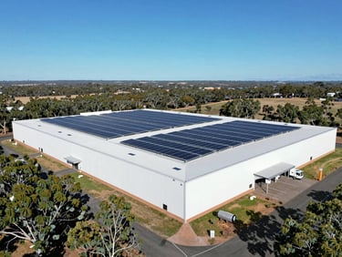 Wide architectural drone shot of a large commercial solar installation on a warehouse roof, clear blue Australian sky, crisp architectural photography, bright Australian daylight, deep eucalyptus greens and clean whites.