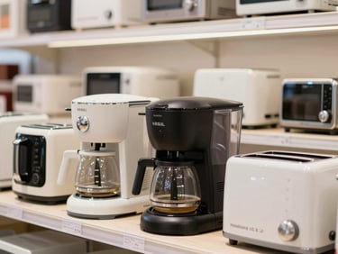 Assortment of small Vestel kitchen appliances (coffee maker, toaster) neatly arranged on a counter in a bright showroom, close-up details.