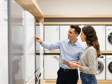 A friendly Vestel showroom staff member assisting a couple with appliance selection, bright clean lighting, modern showroom interior.