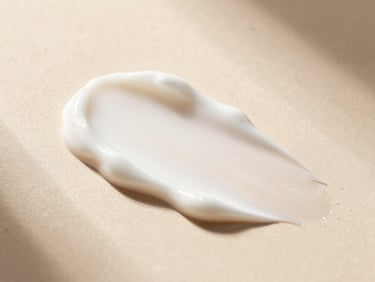 Macro close-up of smooth white cosmetic cream texture on a warm plaster surface, soft morning light, elegant shadows