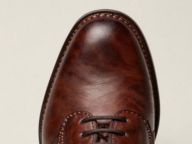 Macro close-up of premium leather shoe sole stitching, welt construction visible, cool diffused studio light on a neutral off-white background, overhead framing