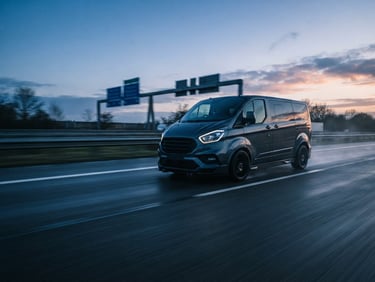 Dynamic low-angle tracking shot of a modern express minivan speeding on a European highway at dawn, cool morning daylight, motion blur, 35mm