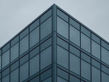 Minimalist architectural photography of a modern glass office building corner, clean geometric steel frame, overcast sky, desaturated blue and slate tones