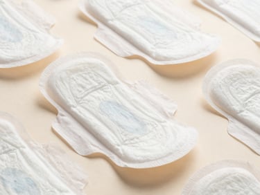 Close-up of unbranded feminine hygiene pads arranged neatly on a warm neutral surface, clinical studio lighting.
