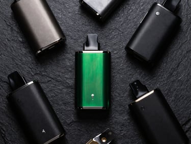 Overhead flat-lay of advanced vape kits and modular devices on dark textured slate, metallic accents, sharp green reflections, 35mm