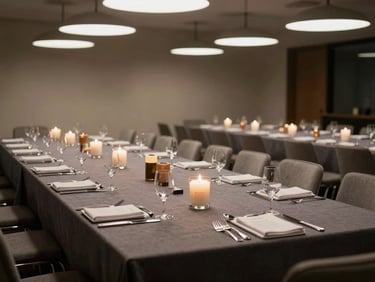 Wide environmental shot of a corporate gala dinner setup — rectangular conference-style tables with dark linen runners, branded centerpiece candles, polished cutlery in precise rows, neutral studio-quality overhead light, no guests