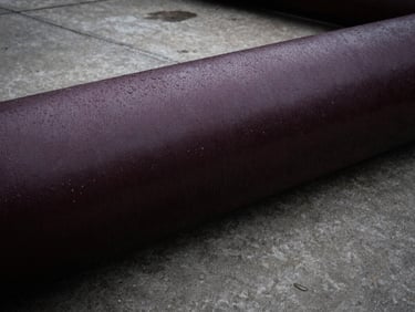 Industrial drainage pipe on a concrete floor, water droplets, high contrast, deep charcoal tones, industrial engineering photography.