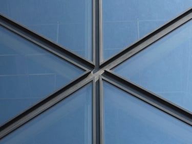 Extreme macro detail of a structural glass curtain wall joint, showing precise metal connections and reflective surfaces under sharp daylight.