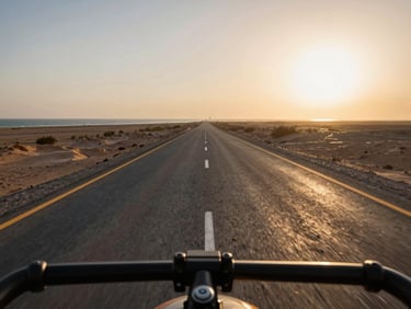 Wide environmental frame from handlebar mount looking ahead on the Makran Coastal Highway, flat open tarmac stretching to the horizon, Arabian Sea glinting at the far left, golden-hour light raking across the road surface from the right
