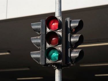 Traffic signal light unit mounted on a metal pole at a parking facility entrance, direct daylight, high contrast, red and green LED lenses visible, weatherproof housing, no people