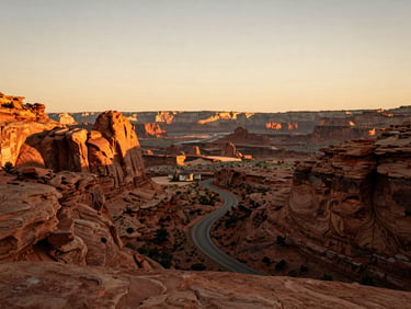 Wide-angle view of red rock canyons under warm golden-hour light, a winding road below, cinematic atmosphere