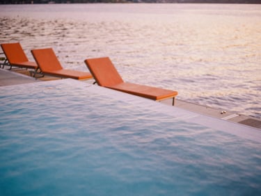 An elegant swimming pool floating on calm lake water, classic orange sun loungers, soft golden light, shallow depth of field, 35mm film.