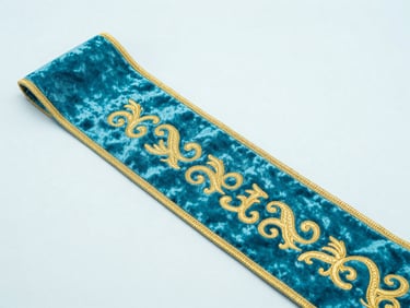 Close-up of a luxurious custom ceremonial sash with gold embroidery on rich velvet fabric, soft cyan studio lighting, high-key product photography