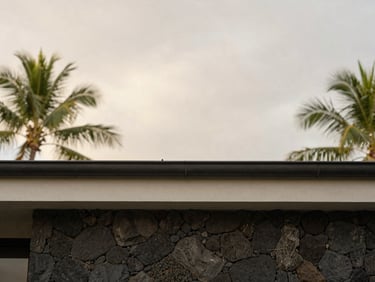 Architectural detail of a minimalist villa roofline and rain gutter against a soft, overcast tropical sky, clean lines, volcanic stone wall