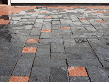 Wide shot of freshly impregnated paving stones, dark and wet, reflecting bright sunlight, against a clean facade, crisp outdoor photography, rich slate gray tones.