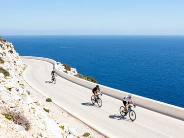 Sunny wide-angle shot of road cyclists riding along a cliffside road in Spain overlooking the deep blue Mediterranean Sea, high-key bright daylight.