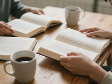Candid close-up of hands holding open books and coffee mugs around a wooden table, soft morning light, warm editorial photography