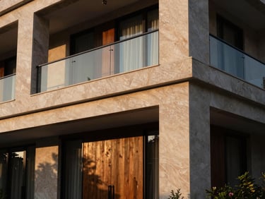 Detalle de una fachada de residencia de lujo moderna, con líneas limpias, materiales nobles como piedra y madera, y una iluminación sutil que resalta la arquitectura.