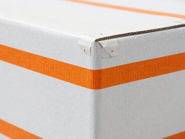 Close-up of double-wall cardboard box corners reinforced with rigid edge protectors in an industrial shipping hub, 35mm