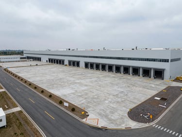 Wide-angle view of a completed automotive logistics facility, large reinforced concrete floor and loading bays visible, overcast daylight, heavy-duty access roads and site markings in foreground, no people, documentary industrial site photography