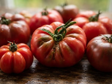 Tight macro shot of fresh heirloom tomatoes on a wooden prep table, soft scandinavian natural light, rich crimson tones, shallow depth of field, 35mm