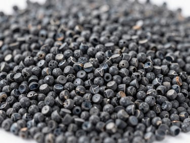 Close-up of perfectly dispersed black masterbatch pellets for blown film, bright industrial light, cool gray tones, macro depth of field