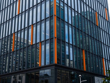 Wide environmental shot of a modern corporate office building exterior, glass facade reflecting city, sharp lines, deep blue tones.
