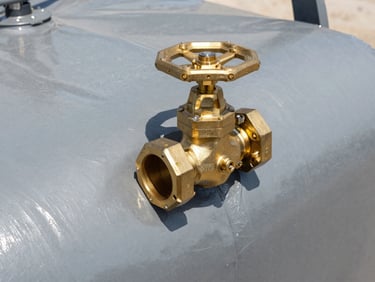 Technical close-up of a heavy-duty brass high-flow valve connection on an Albers Alligator flexible water reservoir, showing the thick grey 1100 g/m² PVC-coated fabric texture under harsh direct daylight.