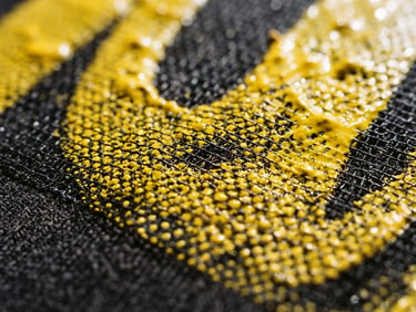 High-contrast macro detail shot of yellow ink pressed through a screen printing mesh, dramatic workshop light, sharp textures, 35mm
