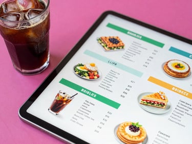 Top-down view of a colorful cafe menu layout on a tablet next to a cold brew glass with condensation, bright natural daylight, magenta accents