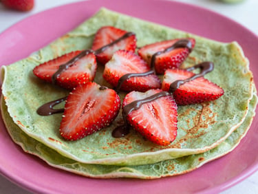 Vibrant close-up of a freshly folded sweet crepe topped with bright red strawberry slices and a drizzle of chocolate, soft natural lighting.