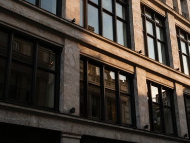 Dramatic low-key architectural detail of a prestigious Mayfair facade, warm golden-hour light reflecting off dark glass windows, 35mm editorial luxury photography