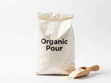 Bright high-key product photography of a clean paper bag of organic wheat flour and a small wooden scoop, crisp white backdrop, sharp focus