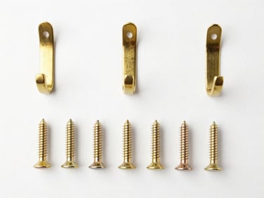 Neatly organized flatlay of solid brass wall hooks and screws, white backdrop, bright studio lighting