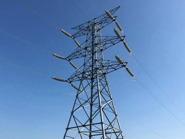 Low-angle heroic shot of a massive steel transmission tower against a crisp blue sky, bright daylight with high contrast, professional industrial photography, sharp focus.